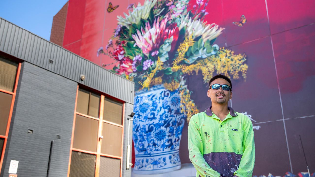 Man in hi-vis shirt stands in front of vibrant floral artwork. 