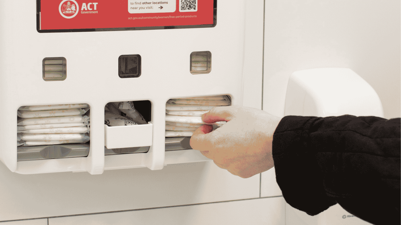 Hand reaches for a sanitary product from a dispenser on a wall. 