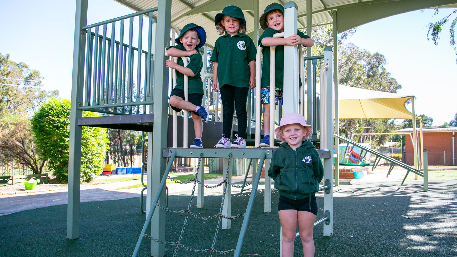 Group of four children stand and climb on play structure smiling for photo. 
