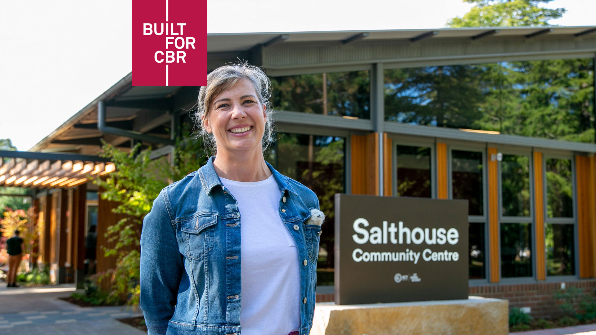 A woman smiles outside a new-looking building. The sign says Salthouse Community Centre.