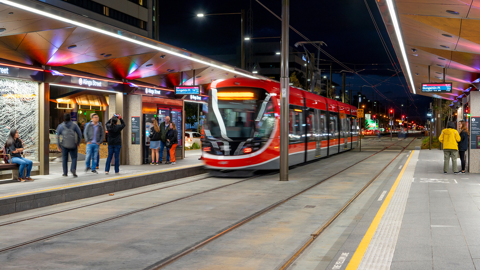 A picture of people standing around a light rail vehicle at night.