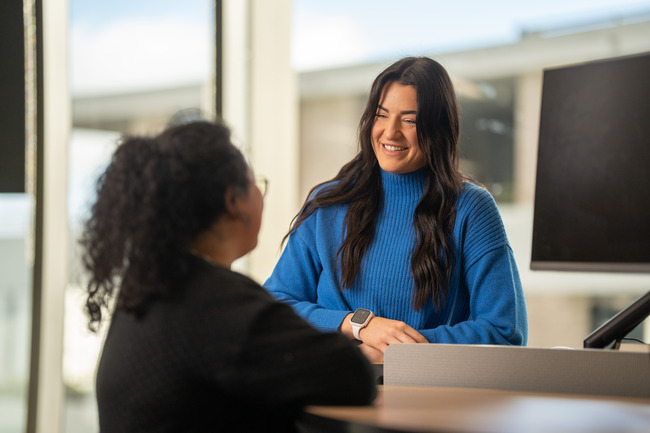 A smiling woman speaks to her colleague. 