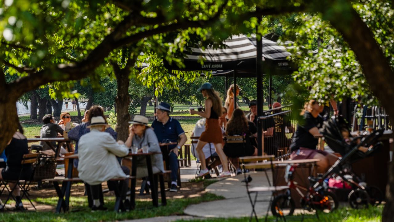 Busy outdoor cafe tables with people, a stroller, bike and shade umbrella.